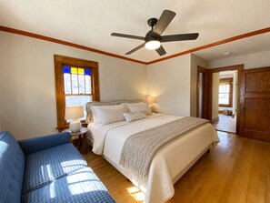 A bedroom with a bed, a ceiling fan, a window with stained glass, a bedside table with a lamp, and a door leading to another room. - Walk to Mayo Clinic! Luxury Furnished 4-bedroom house. Perfect for families (Rochester)
