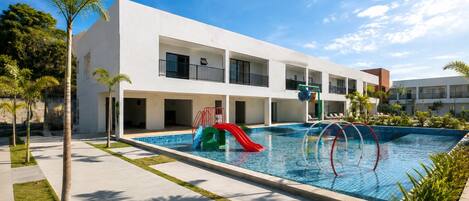 A modern hotel with a swimming pool, a slide, and a multi-story building with balconies.