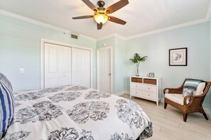 Ein Schlafzimmer mit einem Bett, einem Deckenventilator, einem Schminktisch, einem Sessel und einem gerahmten Bild an der Wand.