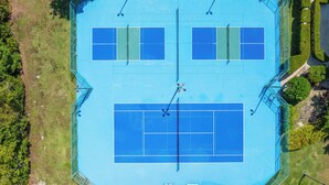 Pista de tenis con valla perimetral, una pista más pequeña contigua y una zona de descanso cubierta.