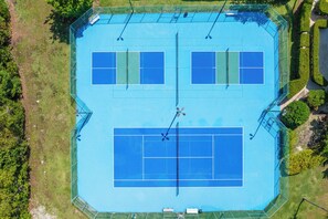 Ein Tennisplatz mit umlaufendem Zaun, ein kleinerer, angrenzender Platz und ein überdachter Sitzbereich.