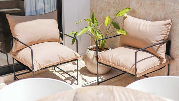Two beige cushioned chairs with metal frames, a potted plant, and a white table on a balcony. - Modern 2BR Retreat in Parques Zama w/ Private Pool (Tulum)
