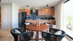 A modern kitchen with wooden cabinets, a black refrigerator, and a dining area with a round table and chairs. - Modern 2BR Retreat in Parques Zama w/ Private Pool (Tulum)