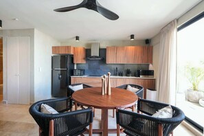 A modern kitchen with wooden cabinets, a black refrigerator, and a dining area with a round table and chairs. - Modern 2BR Retreat in Parques Zama w/ Private Pool (Tulum)