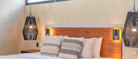 A modern bedroom with a large bed, two bedside tables, a wooden headboard, and hanging pendant lights.