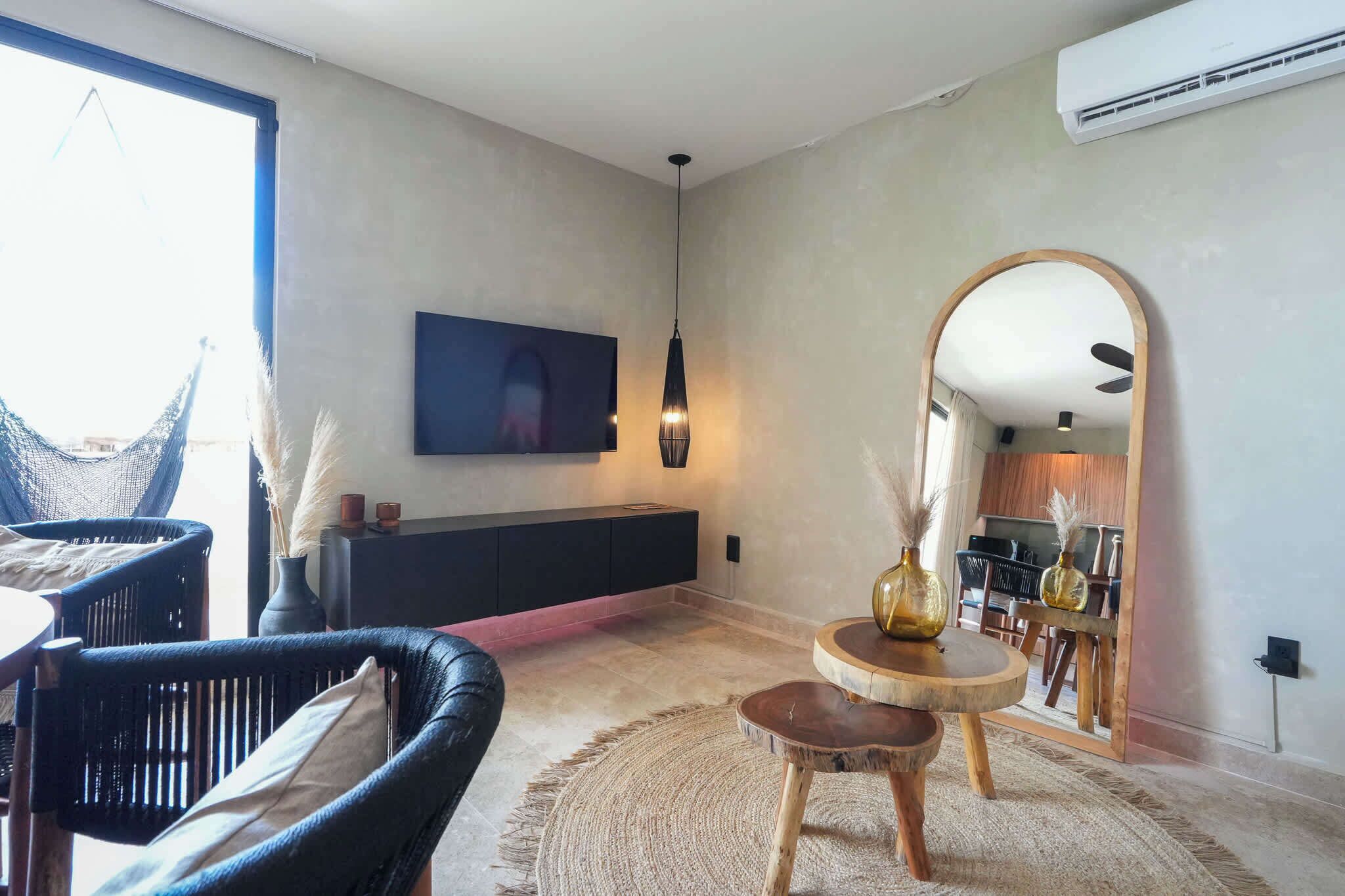 Uma sala de estar moderna com um sofá, uma televisão, uma luminária pendente e um espaço de jantar com cadeiras e uma mesa.