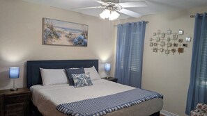 A bedroom with a bed, two bedside lamps, a ceiling fan, a painting, and a wall-mounted mirror. - The Garden Gate Estate, Spacious but Cozy. Near dowtown and highway 25 and 50. (Clermont)