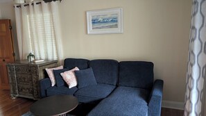 A living room with a dark blue sofa, a small round table, and a decorative cabinet. - The Garden Gate Estate, Spacious but Cozy. Near dowtown and highway 25 and 50. (Clermont)