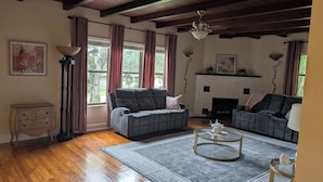 A living room with two grey sofas, a fireplace, a wooden ceiling, and a patterned rug.