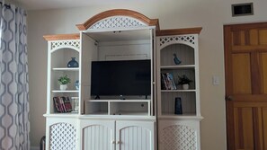 A living room with a TV on a white entertainment unit, a door to the right, and a patterned curtain on the left. - The Garden Gate Estate, Spacious but Cozy. Near dowtown and highway 25 and 50. (Clermont)