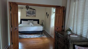 Ein Schlafzimmer mit einem Bett, einer Holzkommode, einem Deckenventilator und einem Fenster mit Vorhängen.