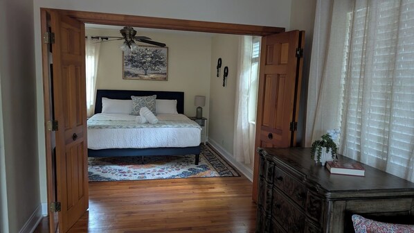 A bedroom with a bed, a wooden dresser, a ceiling fan, and a window with curtains.