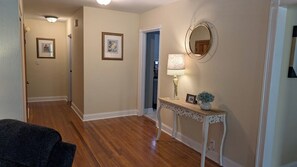 A hallway with wooden flooring, a console table with a lamp and decorative items, and two framed pictures on the walls.