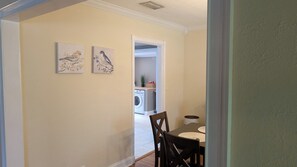 A hallway with a dining area featuring a table and chairs, a washing machine, and two wall-mounted bird paintings.