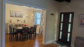 A dining area with a wooden table and chairs, a chandelier, and a window with curtains.