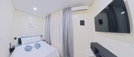 A hotel room with a bed, a TV, an air conditioning unit, and a wall-mounted control panel.