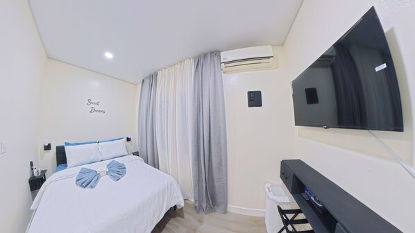 A hotel room with a bed, a TV, an air conditioning unit, and a wall-mounted control panel.