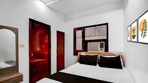 Un dormitorio con cama, cómoda de madera, puerta roja y ventana con aire acondicionado.