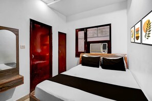 Une chambre à coucher avec un lit, une commode en bois, une porte rouge et une fenêtre équipée d’un climatiseur.