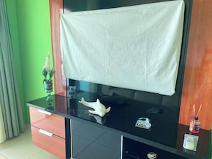 A modern living room with a flat-screen TV mounted on a black cabinet, a decorative white object on the cabinet, and a small plant on the left. - Beachfront apartment (Praia Grande)
