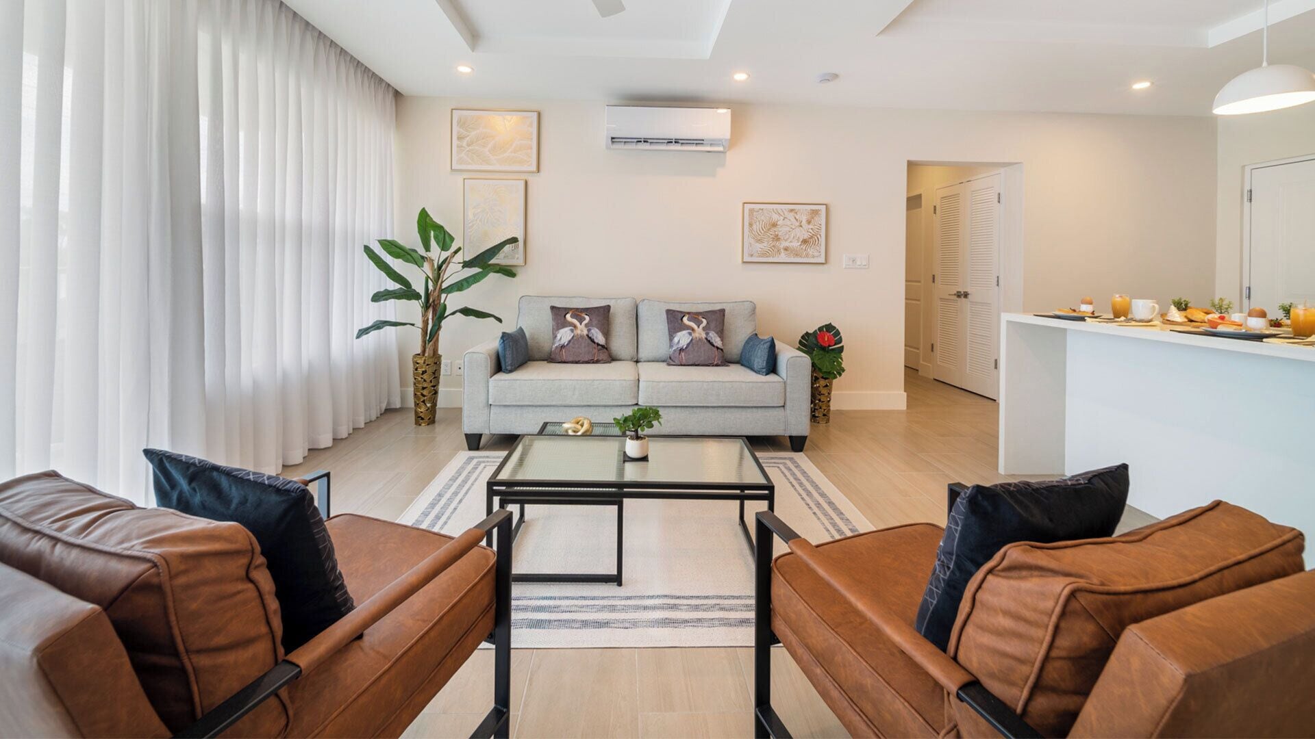 Una sala de estar moderna con un sofá, dos sillones, una mesa de centro y un comedor con alimentos para el desayuno.