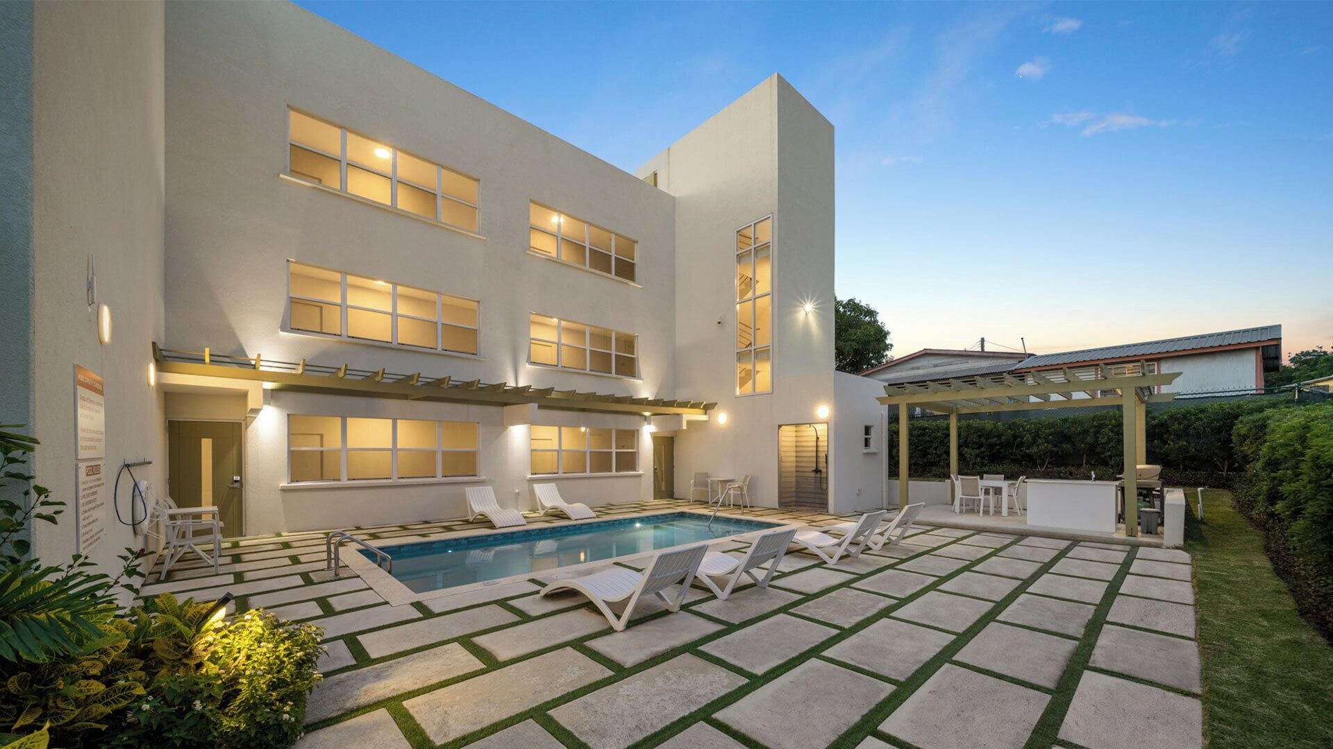 Un edificio moderno con piscina, mobiliario exterior y una pérgola.