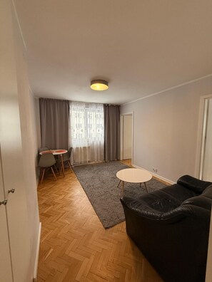 A modern living room with a black leather sofa, a small round table, and a dining area with a table and chairs. - Zlota 3-bedroom apartment in City Center,Pet Friendly (Warszawa)