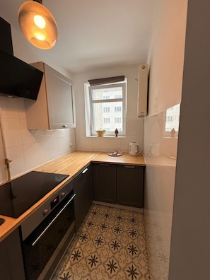 A compact kitchen with a built-in oven, a microwave, and a sink. There's a window with a view of buildings outside. - Zlota 3-bedroom apartment in City Center,Pet Friendly (Warszawa)