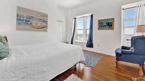 Una camera da letto con un letto, una sedia, due finestre e opere d'arte alle pareti.