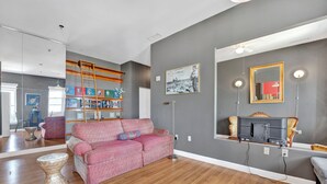 Un soggiorno con un divano rosso decorato, pavimento in legno, una libreria, uno specchio e una ventola a soffitto.