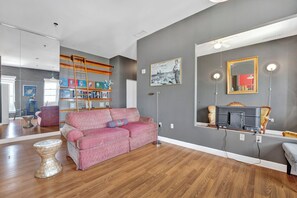Ein Wohnzimmer mit einem rot gemusterten Sofa, Holzboden, einem Bücherregal, einem Spiegel und einem Deckenventilator.
