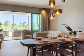 A dining area with a large table set for six, surrounded by chairs, with a view of the outdoors through large windows. - Private Pool Escape - Luminara at The Reef (Willemstad)