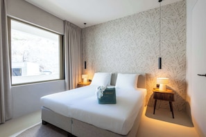 A hotel room with a large bed, two bedside tables with lamps, a window with curtains, and a patterned wall. - Private Pool Escape - Luminara at The Reef (Willemstad)
