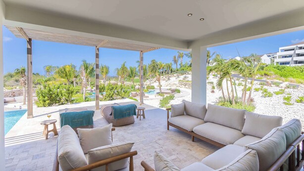 Un espace extérieur moderne, aménagé avec une piscine, des chaises longues et offrant une vue sur un jardin paysager et des bâtiments.