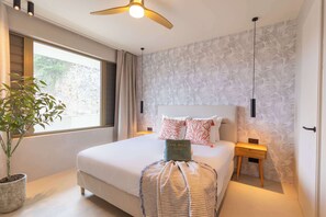 A modern hotel room with a large bed, a ceiling fan, a potted plant, and a view of the outdoors. - Valen 1 | Elevated Caribbean Living at The Reef (Willemstad)