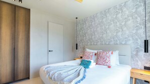 A bedroom with a bed, a wardrobe, a ceiling fan, and a wall with a leaf pattern. - Valen 1 | Elevated Caribbean Living at The Reef (Willemstad)