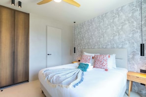 A bedroom with a bed, a wardrobe, a ceiling fan, and a wall with a leaf pattern. - Valen 1 | Elevated Caribbean Living at The Reef (Willemstad)