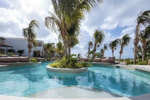 A swimming pool with palm trees, lounge chairs, and a building in the background. - Valen 1 | Elevated Caribbean Living at The Reef (Willemstad)