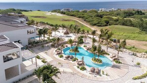 A resort with a swimming pool, palm trees, and a golf course. - Valen 1 | Elevated Caribbean Living at The Reef (Willemstad)