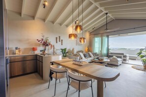 Eine moderne Küche mit Kochinsel, Essbereich mit Holztisch und Stühlen sowie ein Wohnzimmer mit Sofa und Meerblick.