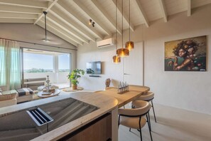 Une cuisine moderne avec un îlot central, des tabourets de bar, une grande fenêtre et un tableau au mur.
