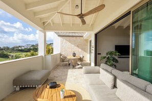 Ein Balkon mit Deckenventilator, eine Sitzecke mit einer Couch und Stühlen, ein Holztisch und ein Blick auf die Landschaft.