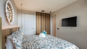 Ett hotellrum med en säng, en platt-TV som är monterad på väggen, en dörr och en taklampa.