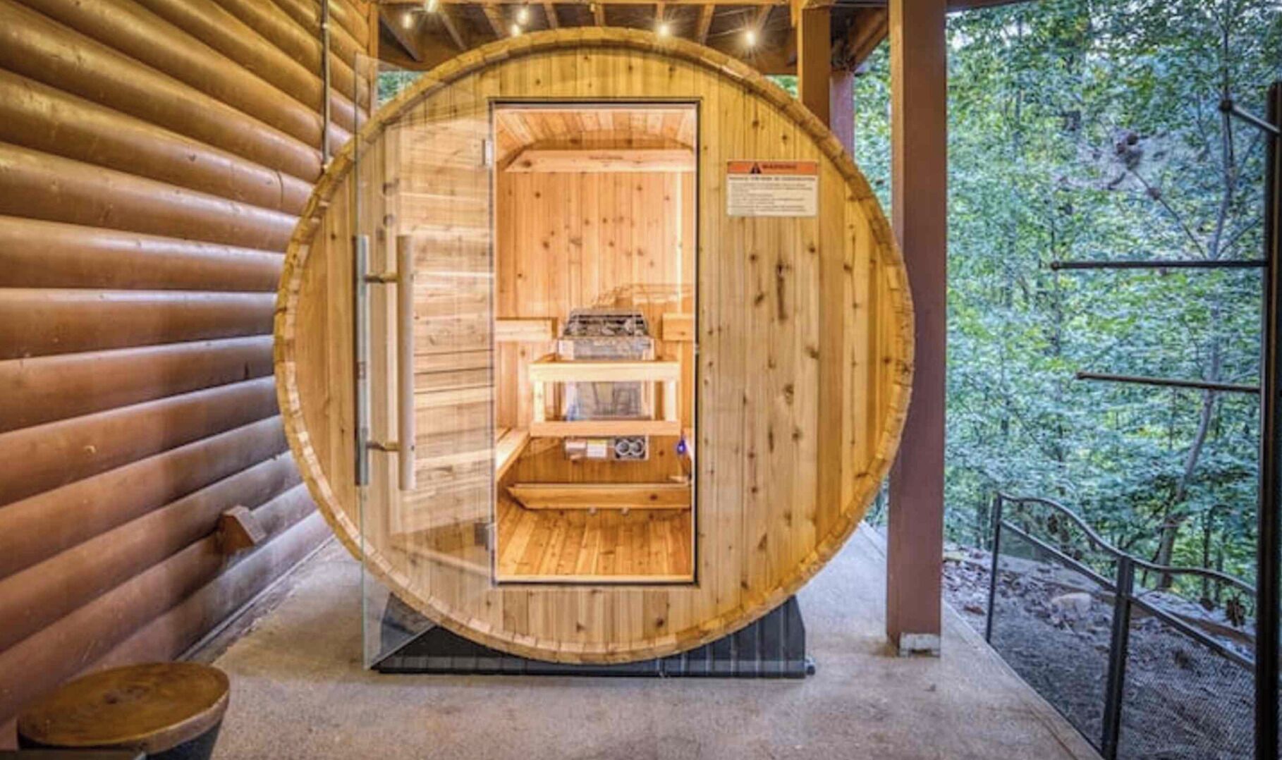 Un sauna en bois avec une porte en verre, un banc à l’intérieur et une vue sur la forêt par la porte.