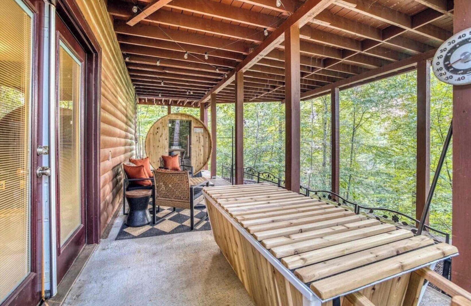 Une terrasse en bois avec un banc et une table, entourée d’une structure de cabane en bois dotée de grandes fenêtres.