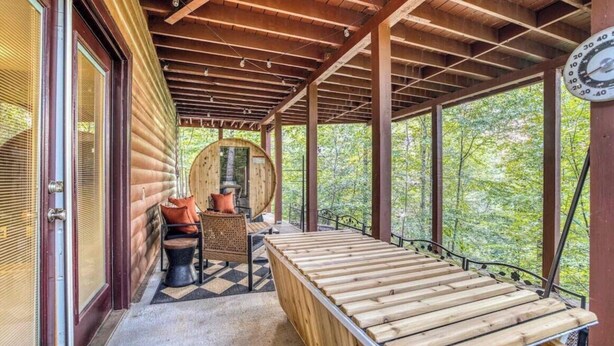 Eine Holzterrasse mit einer Bank und einem Tisch, umgeben von einer Holzhütte mit großen Fenstern.