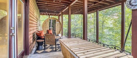 Una terraza de madera con un banco y una mesa, rodeada por una cabaña de madera con ventanales grandes.