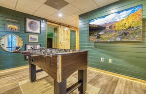 A room with a foosball table, framed pictures on the walls, and a large landscape painting. - Ellijay Luxe Cabin: Hot Tub~Sauna~Cold Plunge (Ellijay)