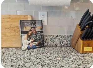 Una encimera de cocina con un libro de recetas, un bloque de cuchillos y una tabla de cortar de madera.