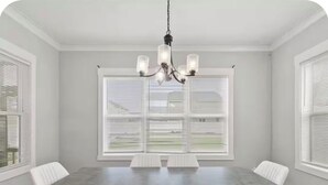 A dining room with a large table, white chairs, a chandelier, and windows with blinds.
